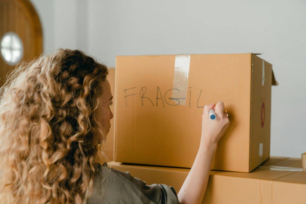 a woman writing "FRAGILE" on a box